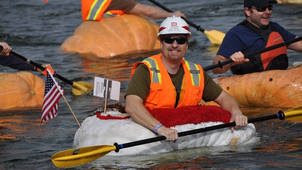 Participants paddling giant pumpkins in a lake during the Pumpkin Regatta, one of the strangest sports in the USA.