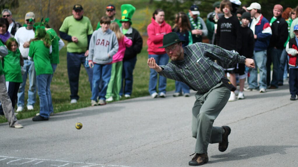A player aiming a shot in Irish Road Bowling along a rural road, a niche forgotten sport.