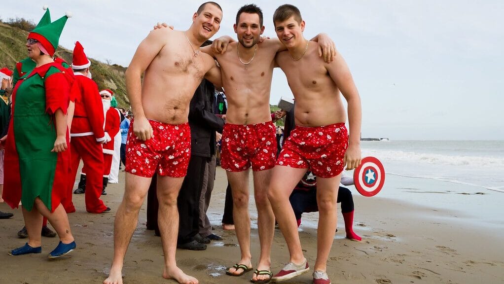 Participants in festive costumes taking part in the Boxing Day Dip, a popular UK festive sporting tradition, as they plunge into icy waters at the beach.