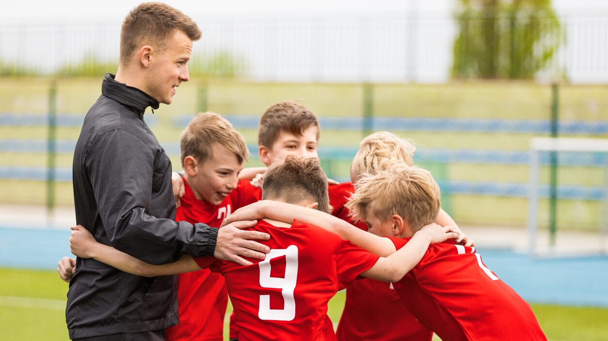 A grassroots coach shaking hands with an opposing coach after a match, teaching players about sportsmanship.