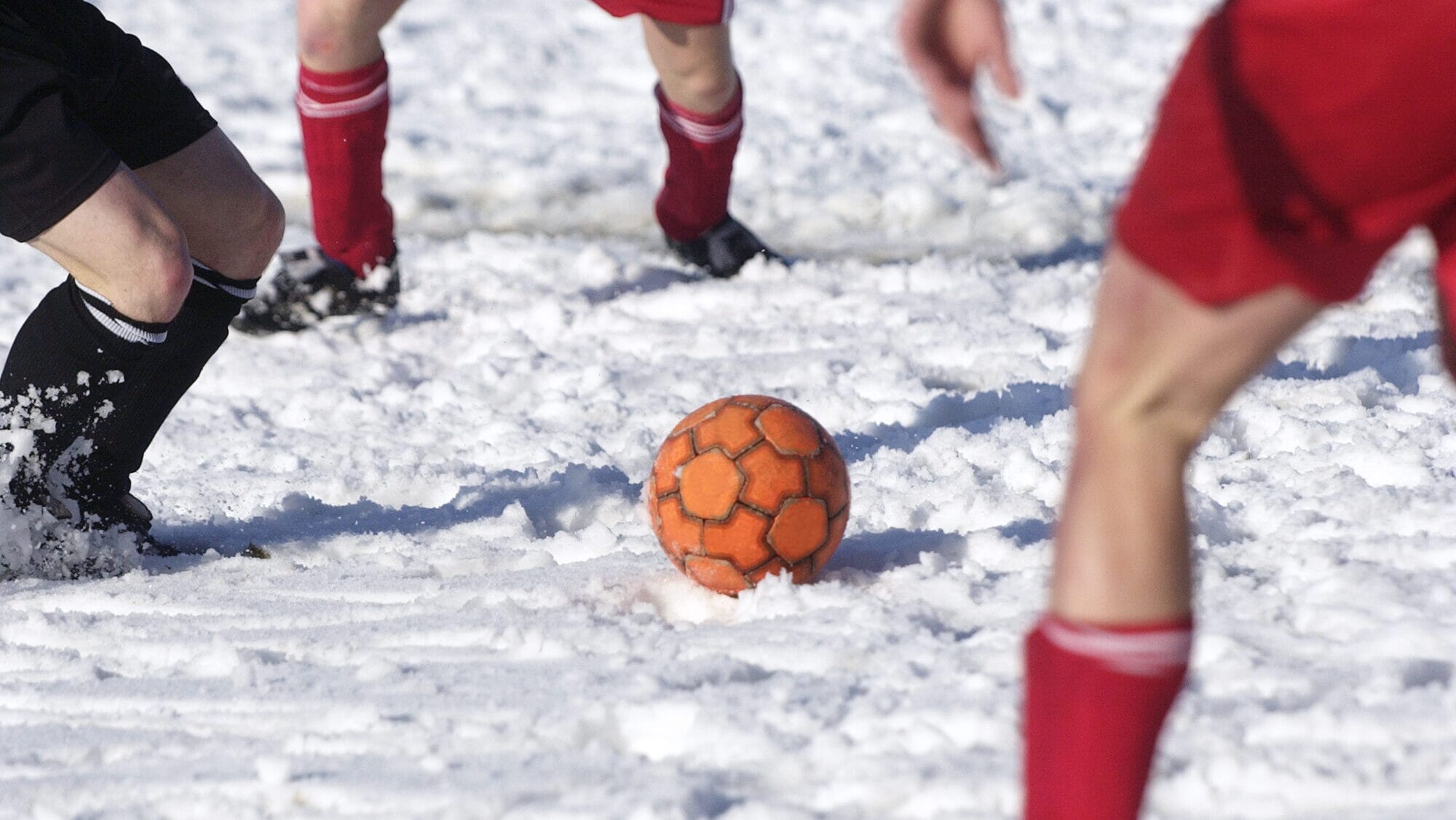 Et lag spiller fotball i snøen iført snøsko og festlige kostymer.