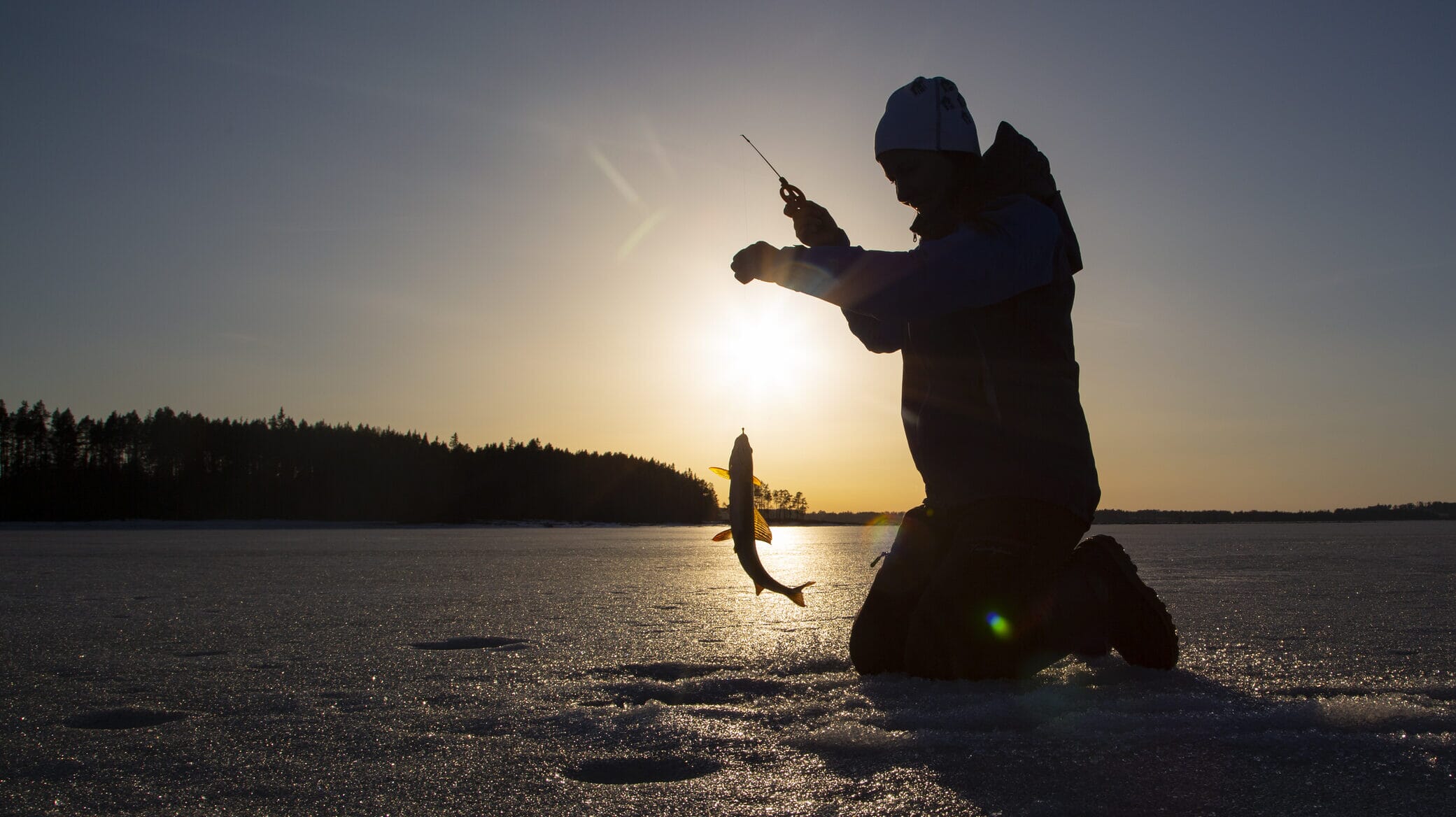 Folk samles på en islagt innsjø for isfiske med julepynt og varme drikker.